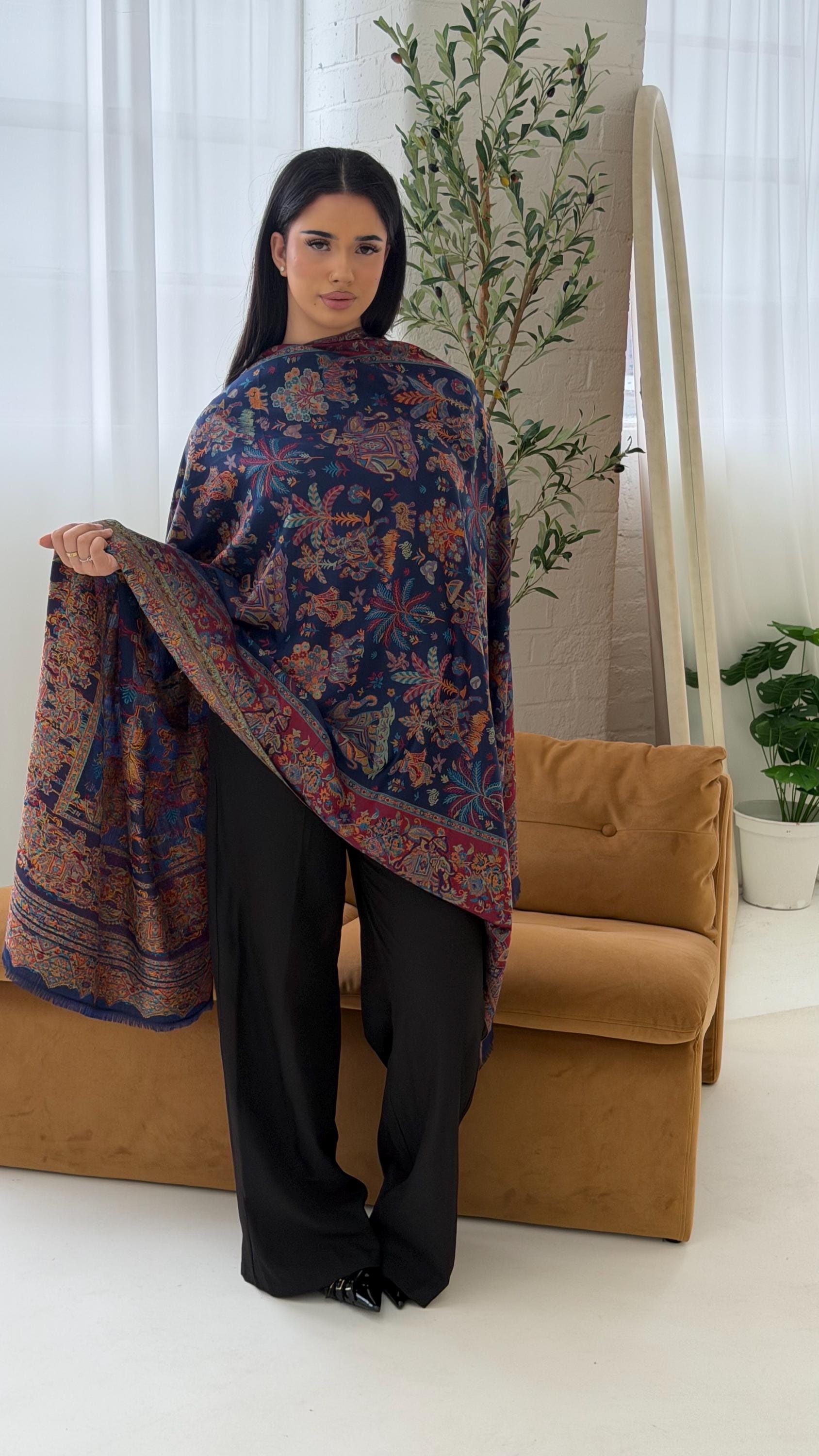 Woman holding a blue patterned pashmina shawl scarf in a room with a couch and plants