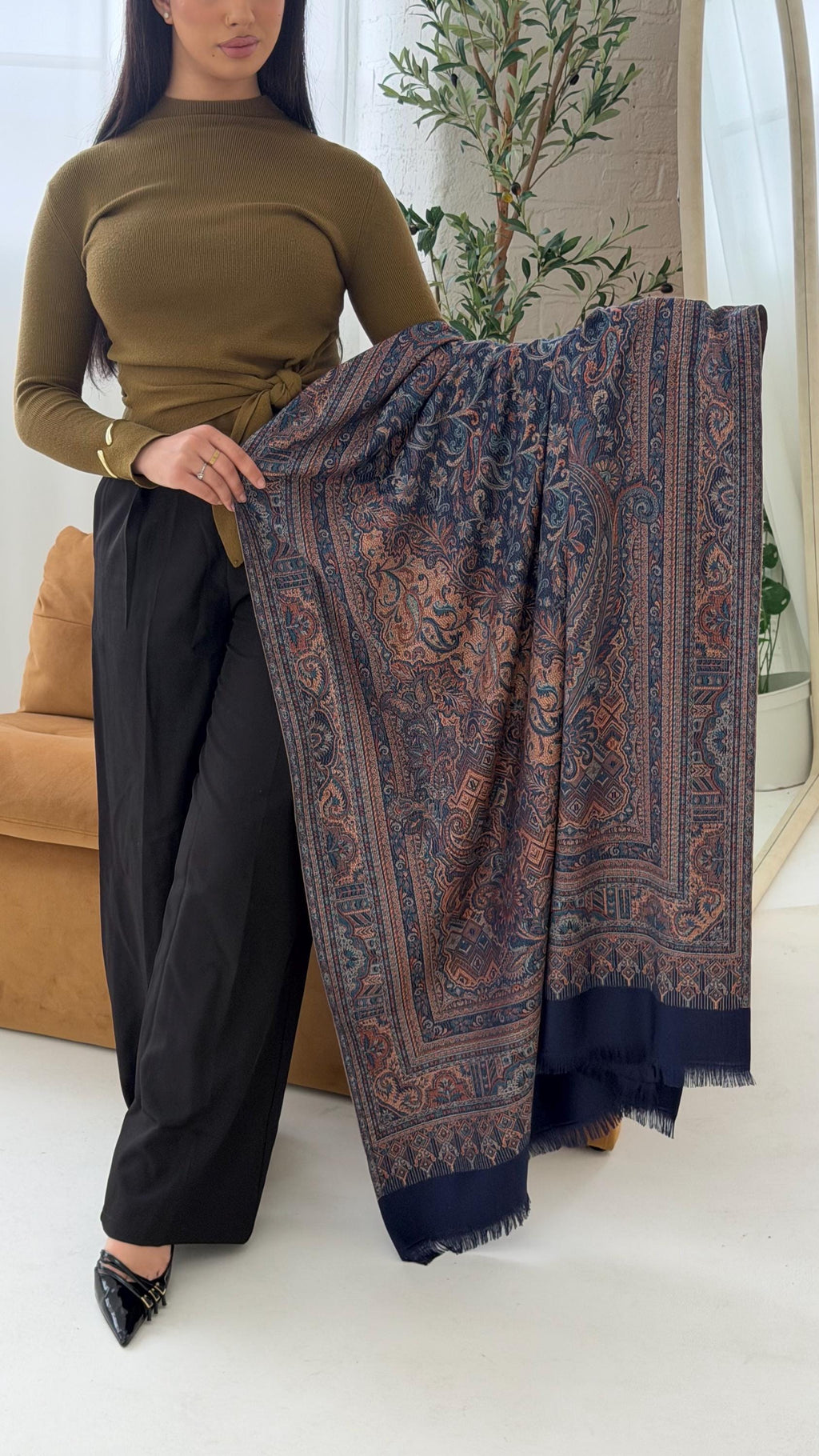 Woman holding a blue scarf in a room with a couch and plant.