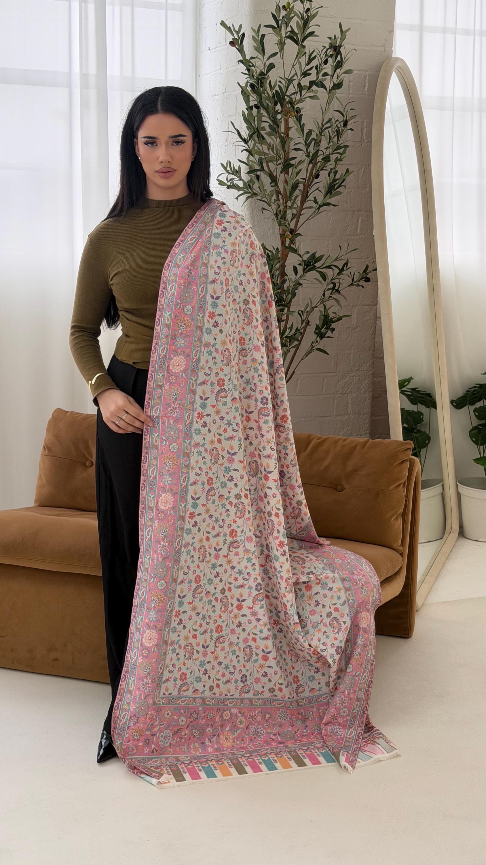 Woman holding a floral pink shawl in a room with a couch and plant.