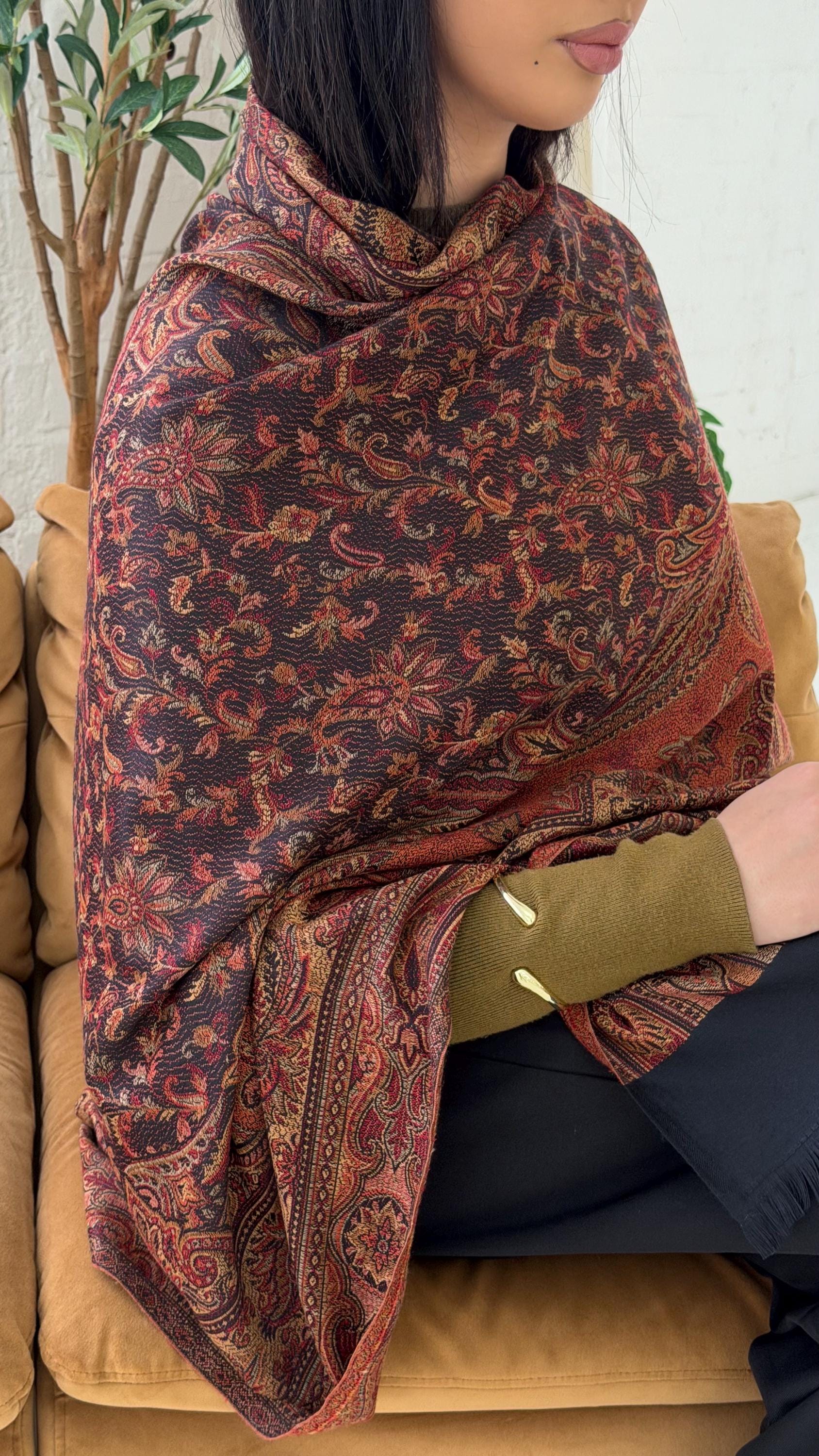 Person wearing a black pashmina patterned shawl sitting on a couch.