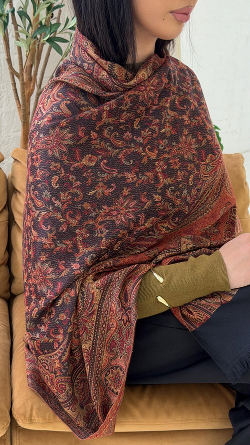 Person wearing a black pashmina patterned shawl sitting on a couch.