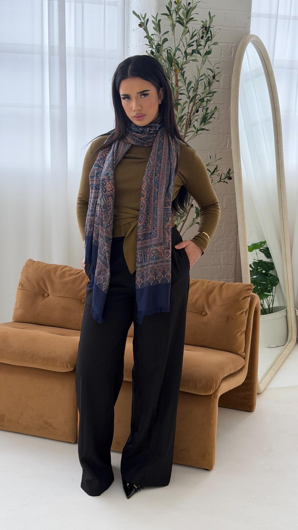 Woman wearing a blue scarf in a minimalistic room with a brown couch and white curtains.