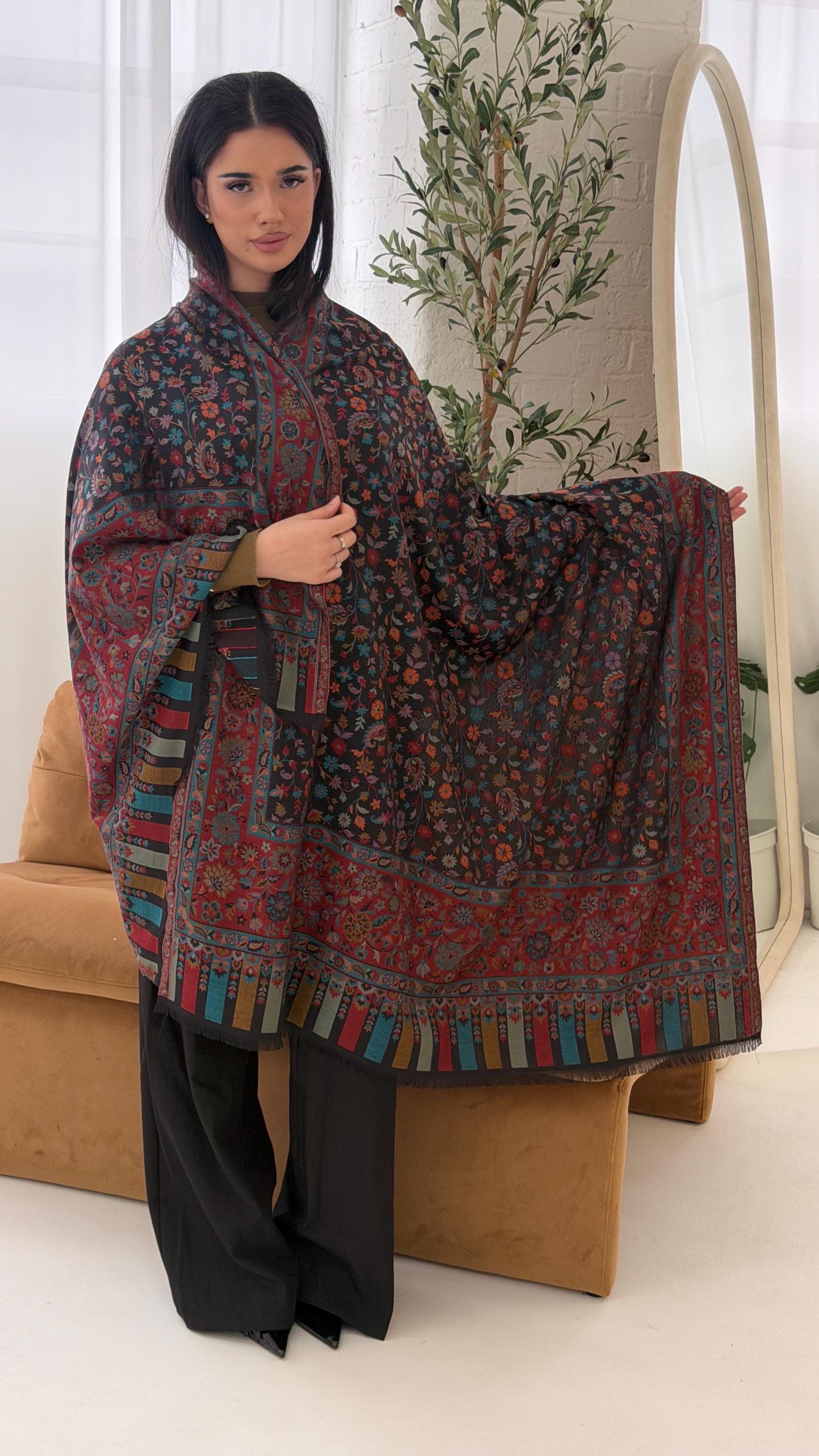 Woman holding a patterned scarf in a room with a plant and beige chair.