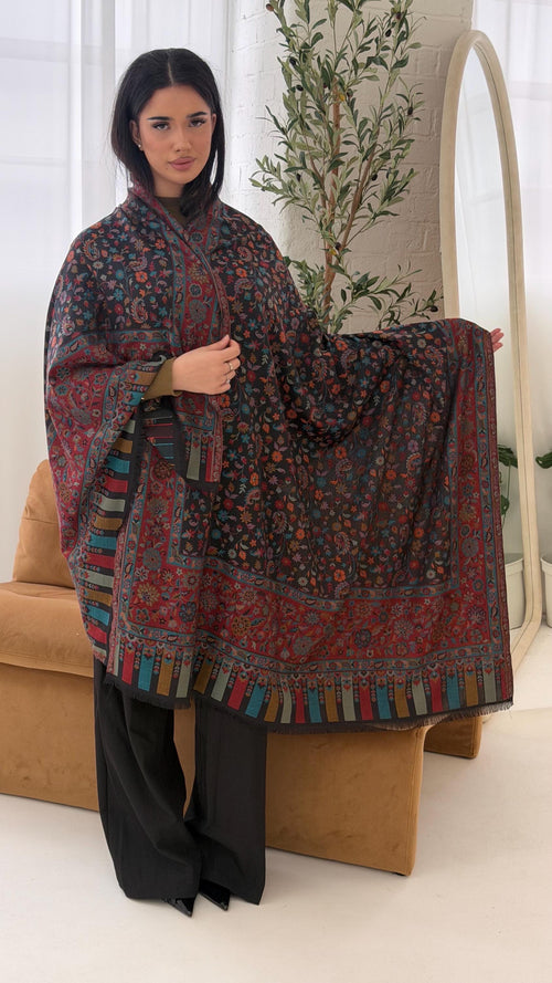 Woman holding a patterned scarf in a room with a plant and beige chair.