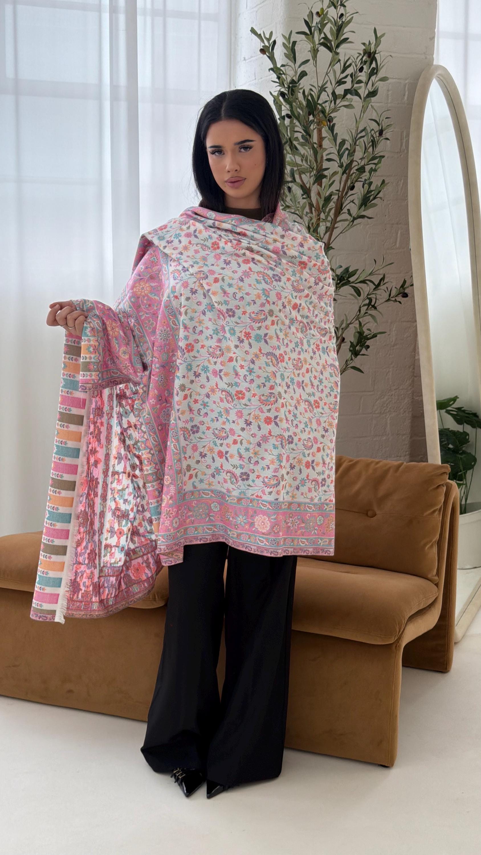 Woman holding a white and pink floral patterned shawl in a room with a couch and plants.