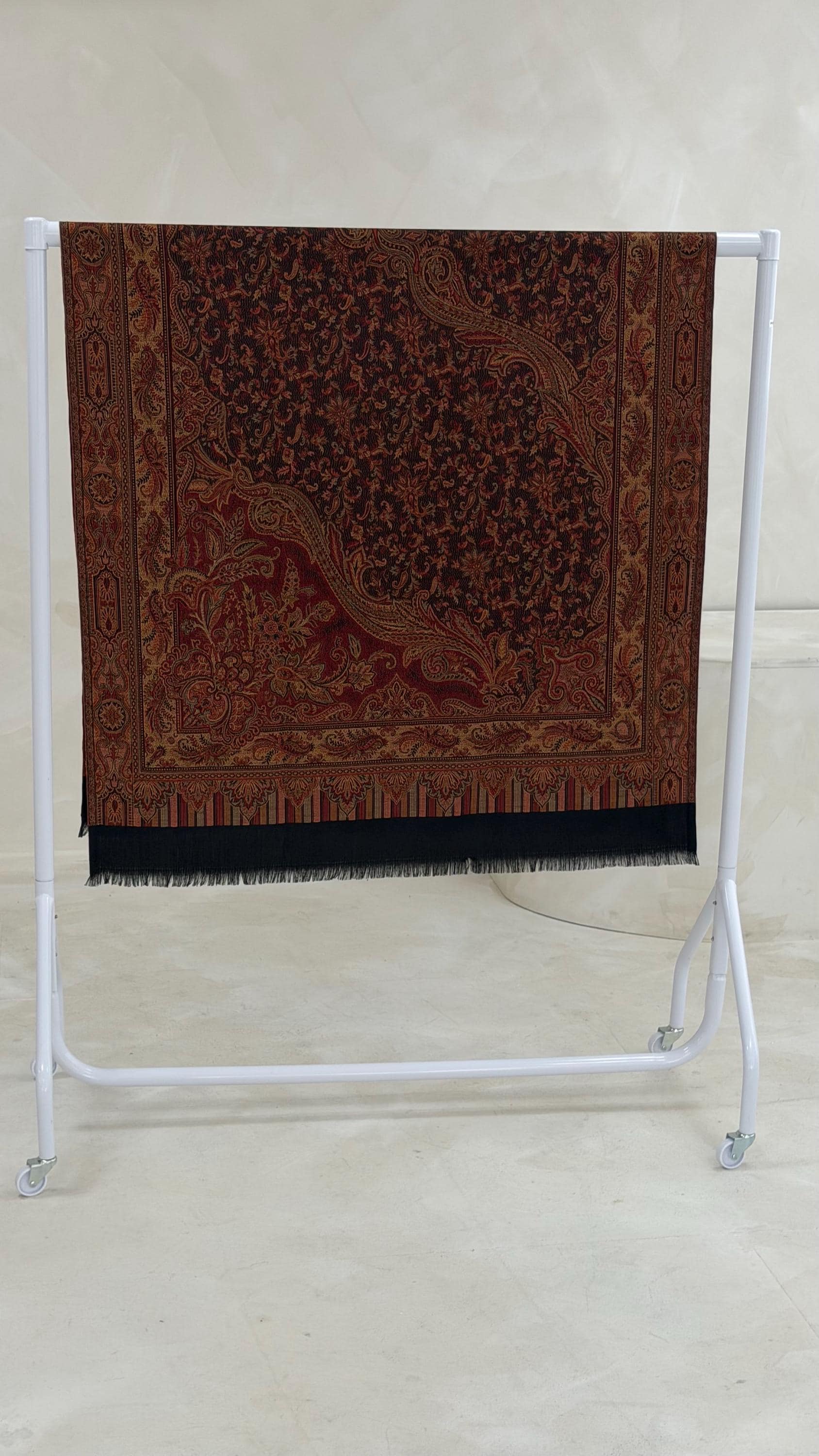 black pashmina patterned shawl scarf on a white stand against a light background