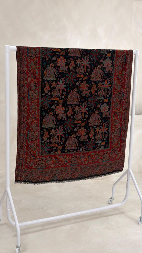 black patterned pashmina shawl scarf with intricate patterns on a white stand against a light background