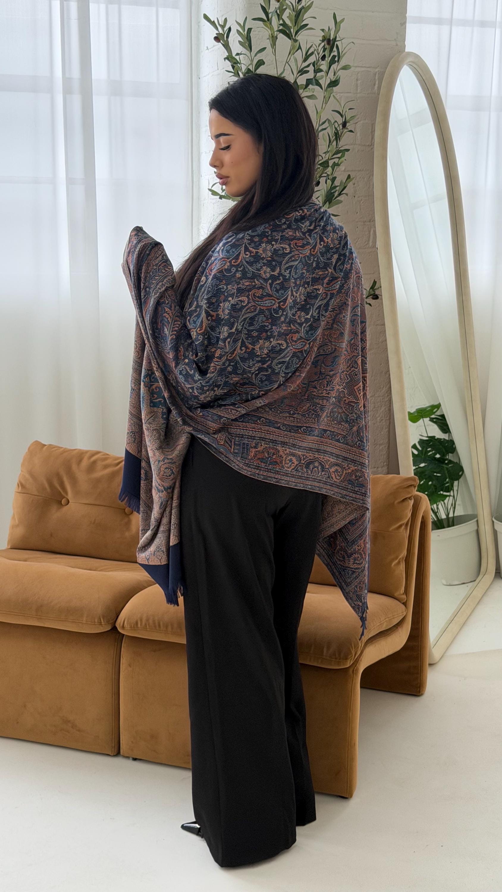 Woman wearing a blue shawl in a room with a couch and plants.